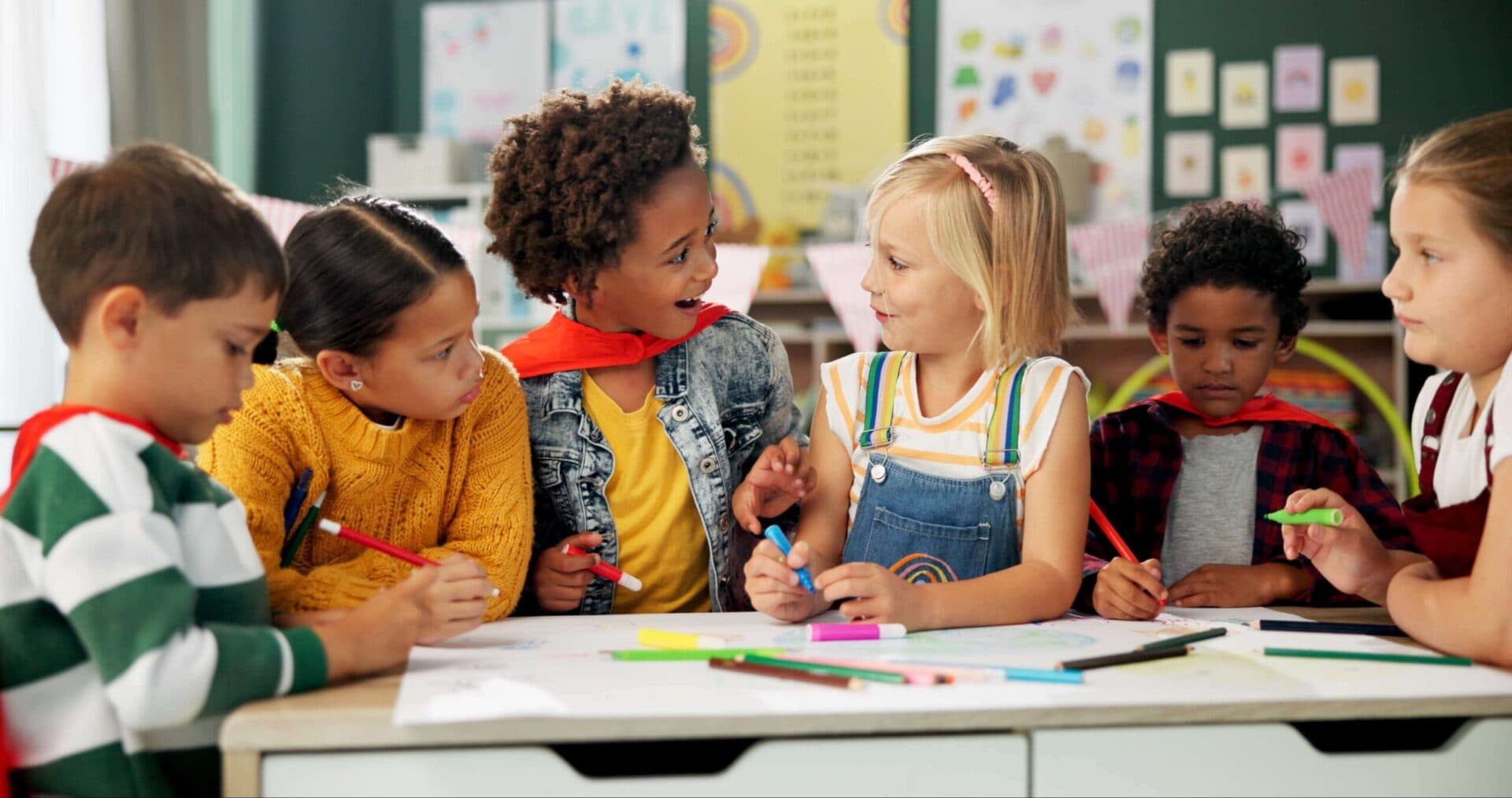 Six children drawing together with markers and colored pencils at a classroom table